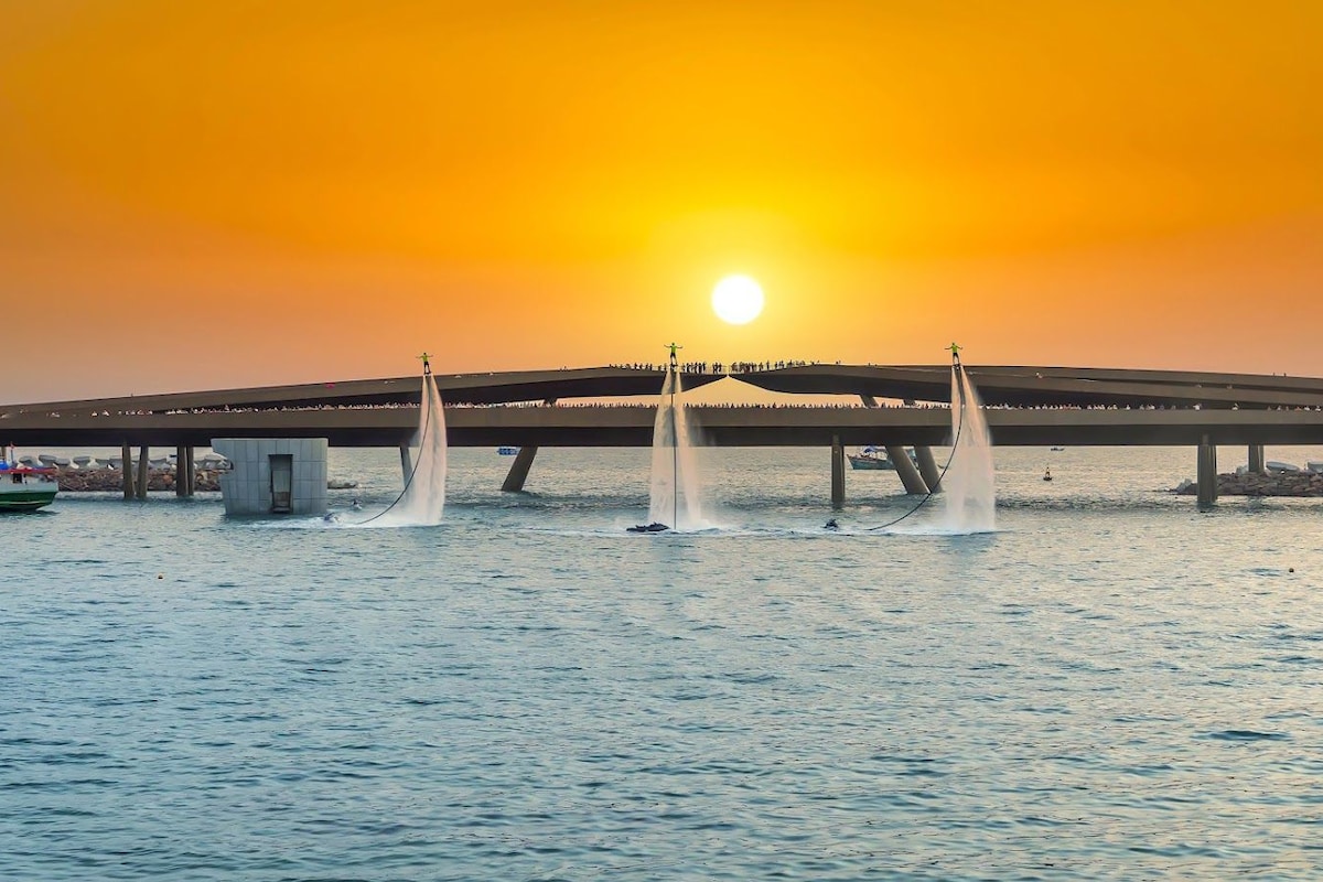 A bridge with water jets, a boat, and a sunset.
