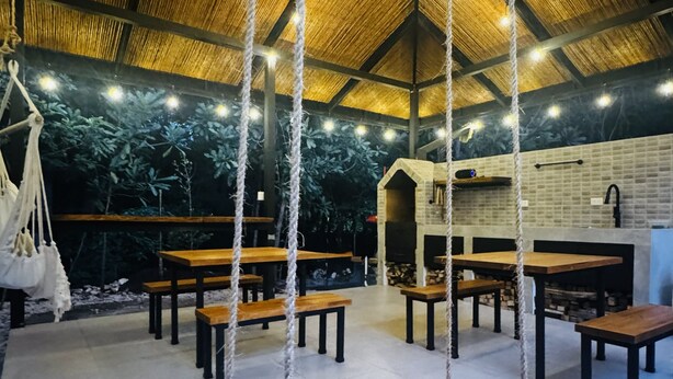 Un interior rústico con mesas y bancos de madera, un columpio colgante y un techo de paja.