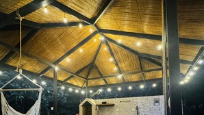 Un espacio de comedor al aire libre con techo de paja, luces colgantes y pared de ladrillo con un lavamanos.