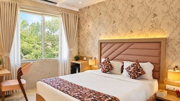 A hotel room with a large bed, a desk, a chair, and a window with curtains.