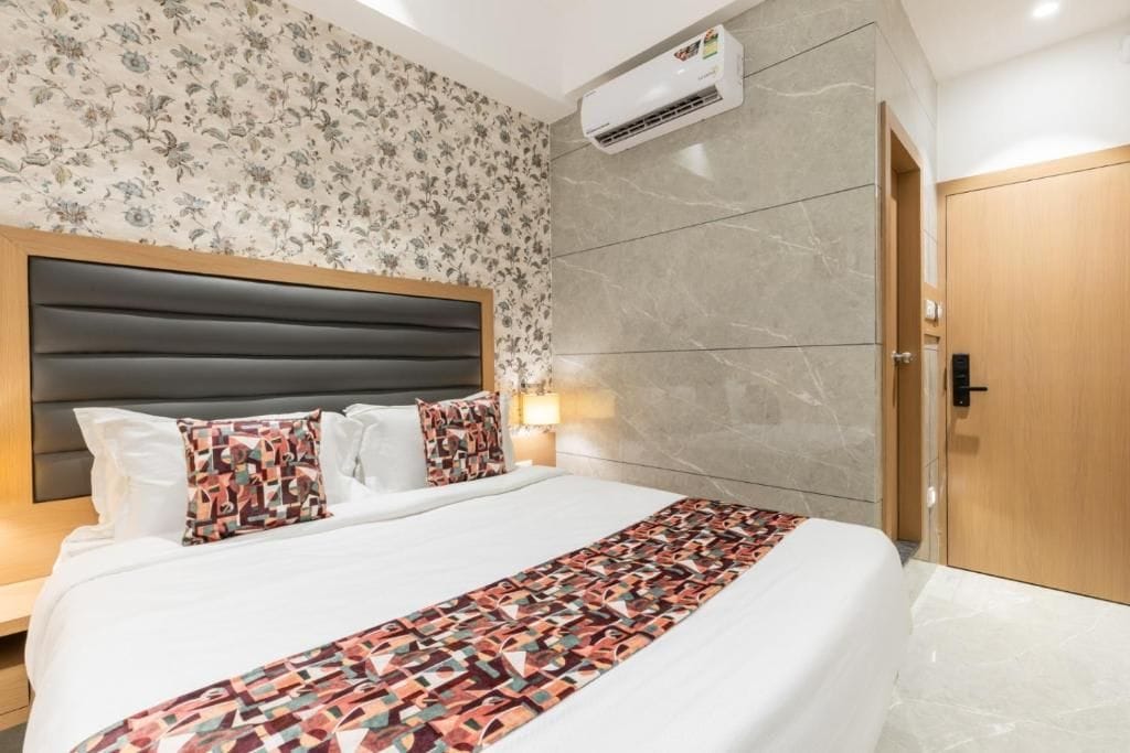 Una habitación de hotel con una cama grande, un cabecero, papel tapiz floral y una pared de mármol, además de un equipo de aire acondicionado.