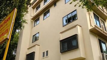 Un edificio de varios pisos con unidades de aire acondicionado, un cartel y un seto verde.