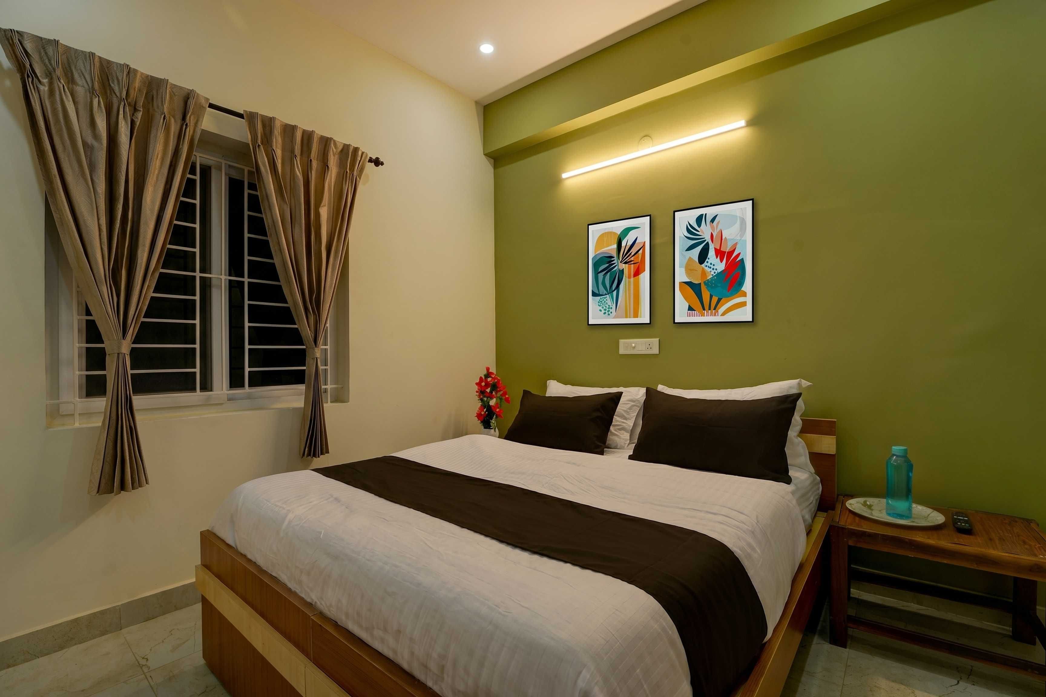 Habitación de hotel con cama, cortinas, mesita de noche, un jarrón de flores y dos obras de arte en la pared.