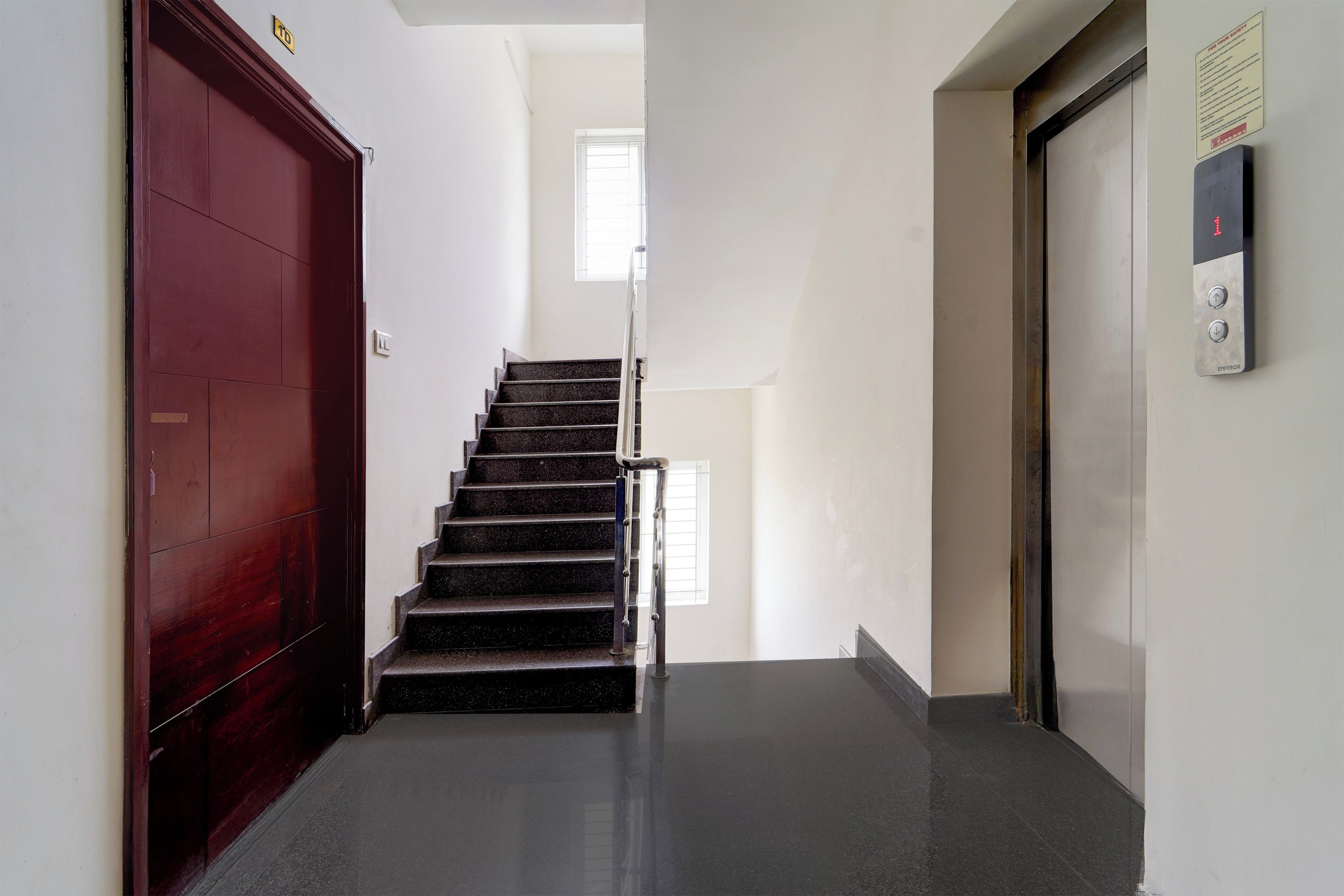 Una escalera con una puerta roja a la izquierda y un ascensor a la derecha.
