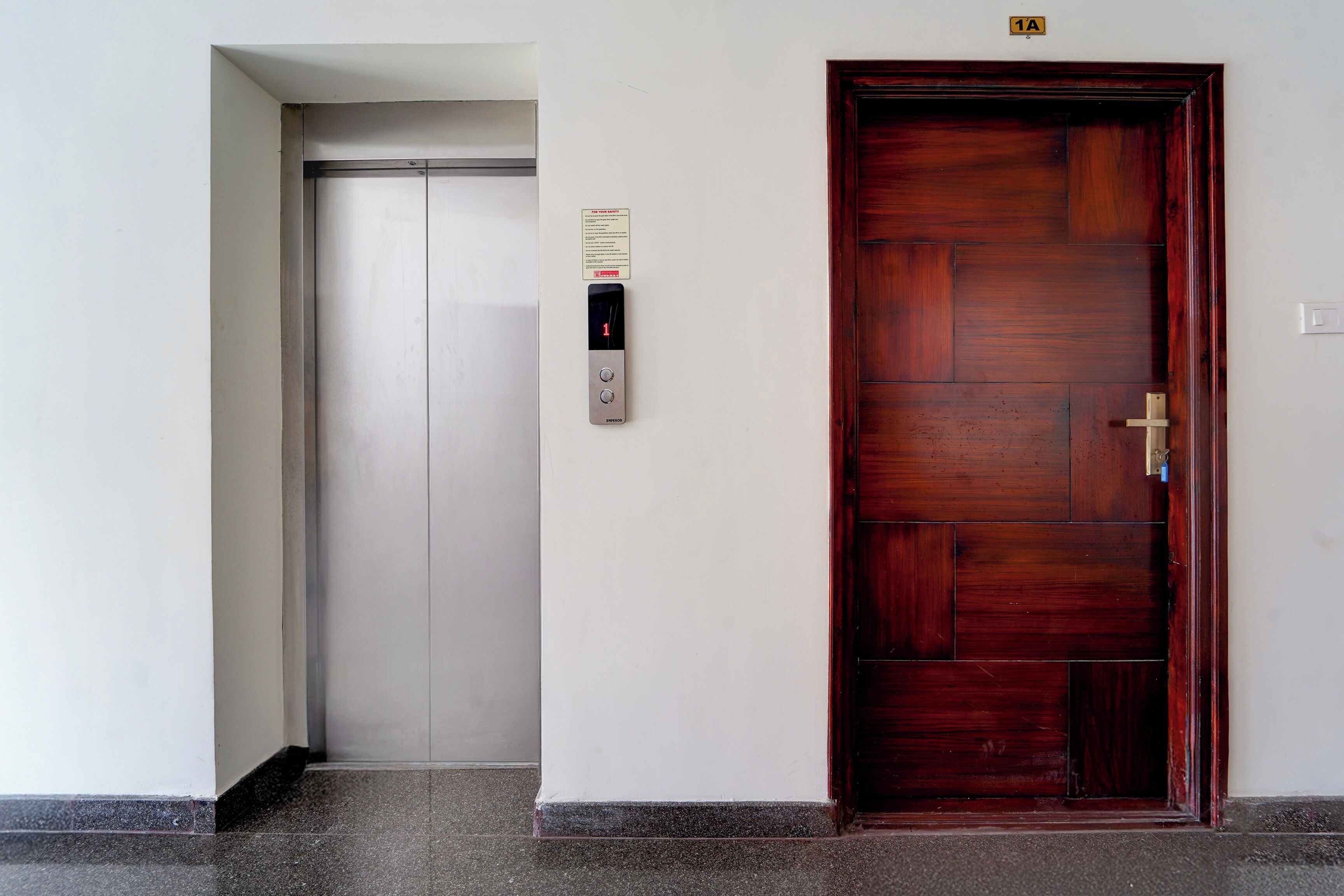 Un ascensor con pantalla digital y puerta de madera con tirador de latón.