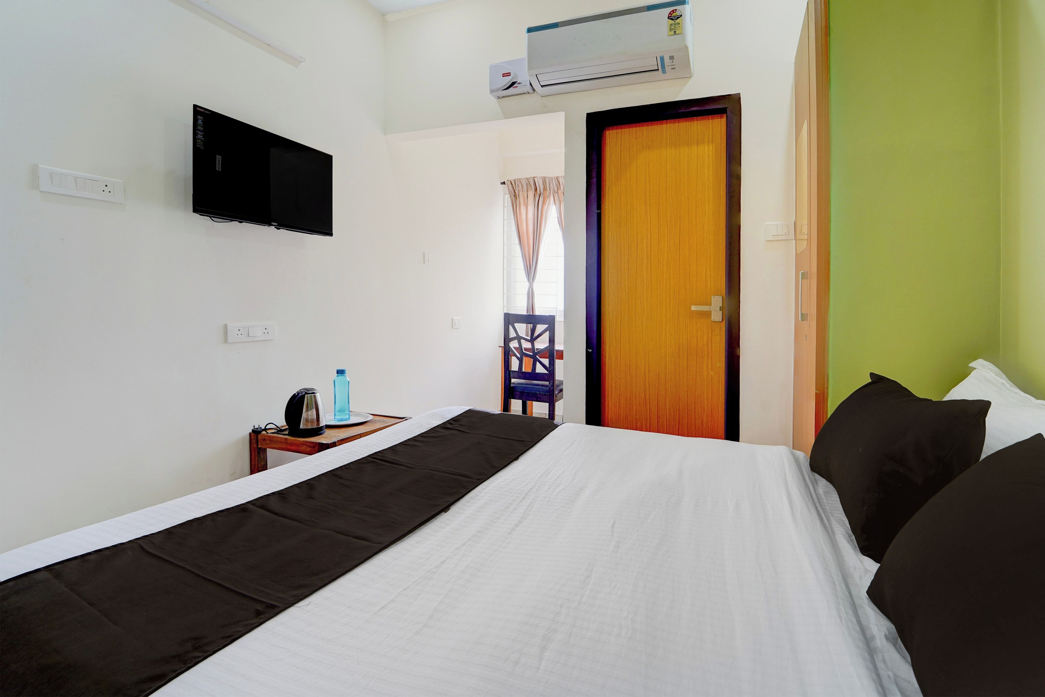 Habitación de hotel con cama, televisión, aire acondicionado, ventana con cortinas y puerta.