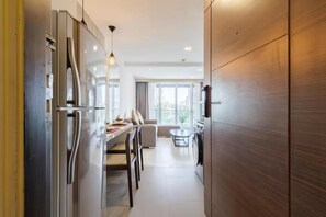 A modern kitchen with a built-in refrigerator, a dining area with a table and chairs, and a view of the outdoors through large windows. - Shine 43 Service Residence Bangkok (Krung Thep Maha Nakhon)