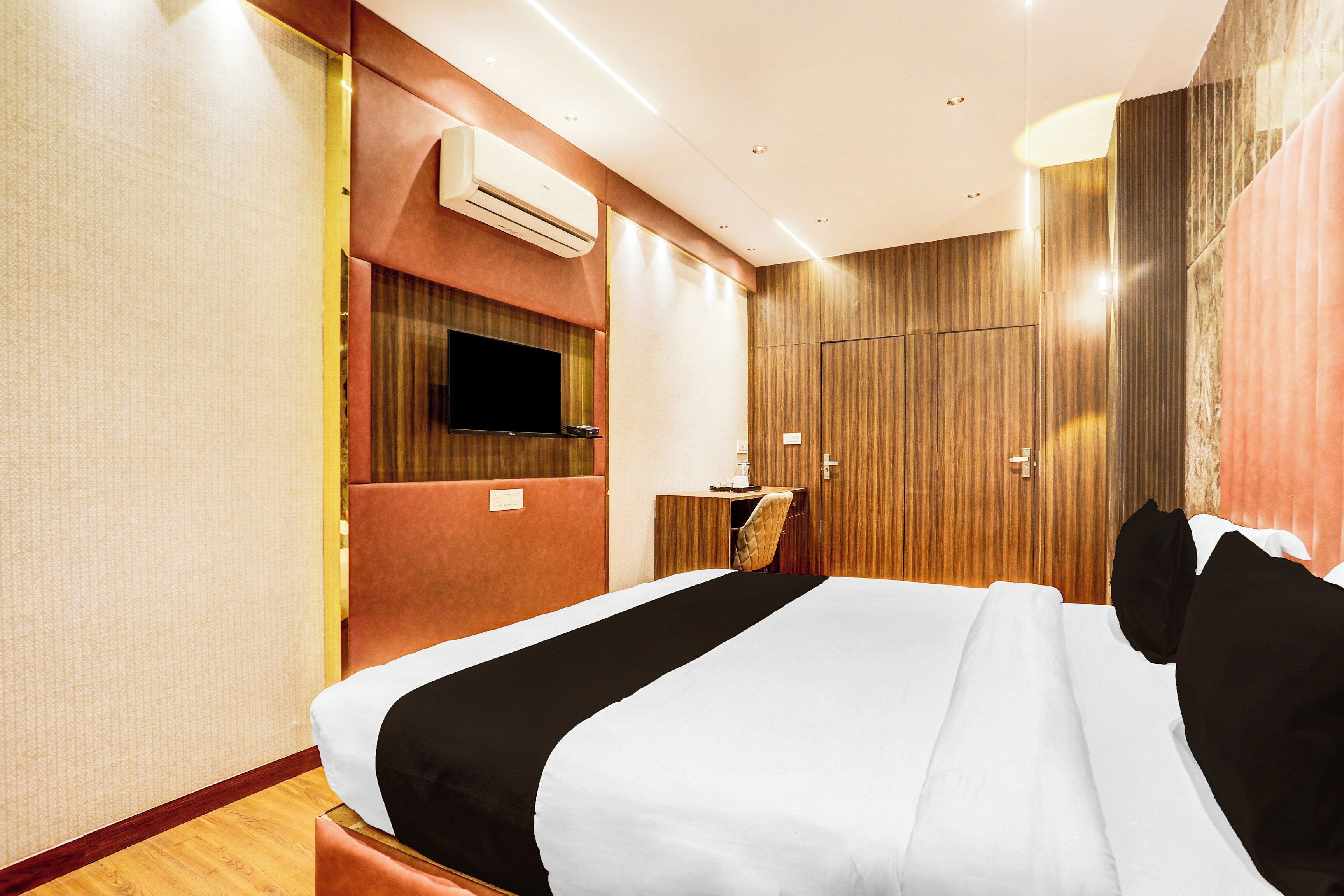 A hotel room with a large bed, a flat-screen TV mounted on the wall, and a wooden wardrobe.