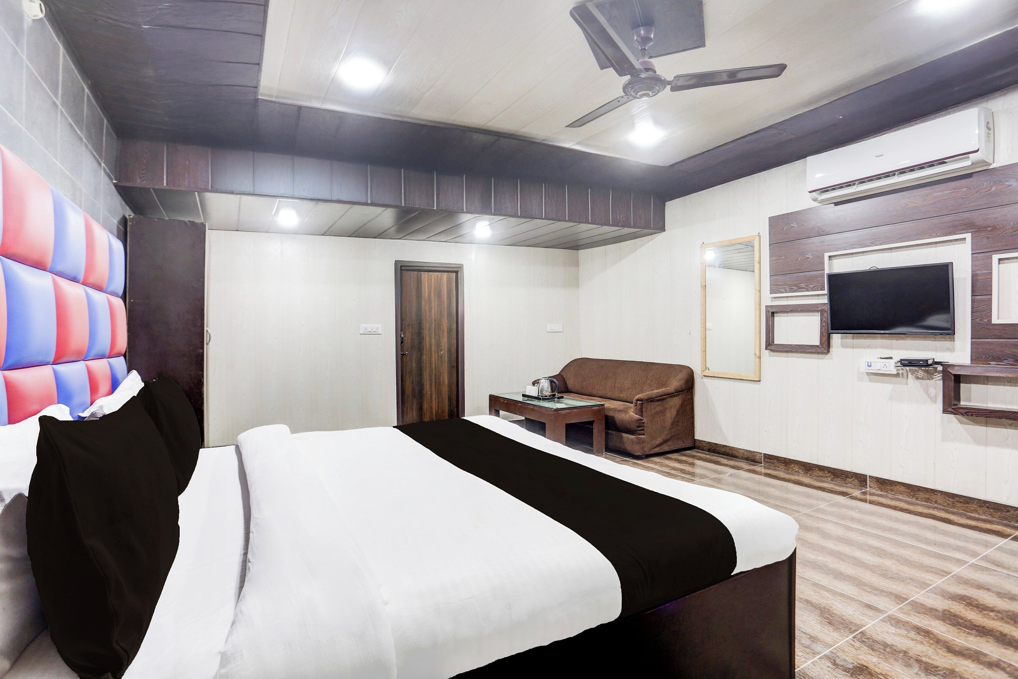 Quarto de hotel com cama, escrivaninha, cadeira, televisão e ventoinha no teto.
