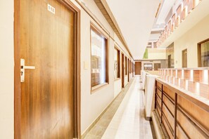A hotel corridor with wooden doors and windows, a tiled floor, and a railing on the right. - Townhouse by OYO Haibowal Chowk Near DMC (Ludhiana)