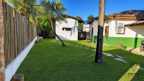Un jardí ben cuidat amb gespa, una tanca de fusta, una palmera i un edifici blanc amb base verda.