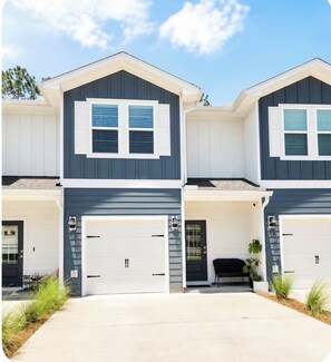 A two-story residential building with a garage, a covered porch, and a small outdoor seating area. - Family friendly Santa Rosa Beach housenear 30A (Santa Rosa Beach)