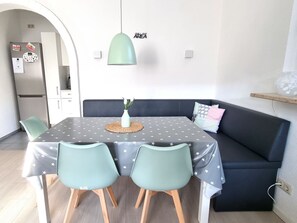 Un comedor con una mesa dispuesta para cuatro, un sofá oscuro y una lámpara colgante.