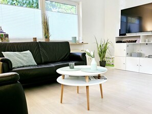 Una sala de estar moderna con un sofá de cuero negro, una mesa de centro blanca y un televisor sobre un mueble.