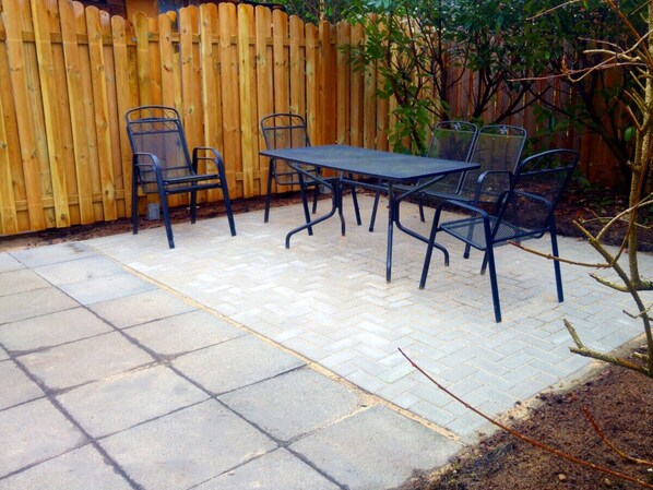 Un patio con una mesa, sillas, una valla de madera y un árbol.