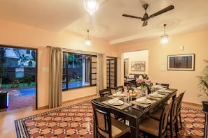 A dining area with a table set for four, a ceiling fan, and a view of a pool outside. - Galeria  Portuguese style 4bhk Pvt Pool (Arpora)