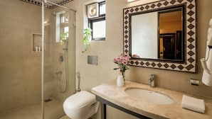 Un baño con cabina de ducha de vidrio, inodoro, lavamanos con espejo y un florero con flores.