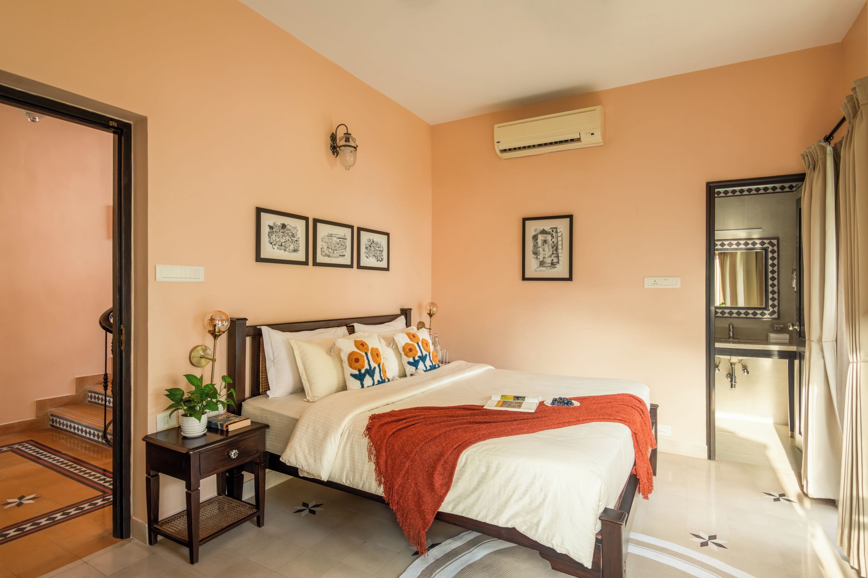 Un dormitorio con cama, mesitas de noche, aire acondicionado de pared y cuadros enmarcados.