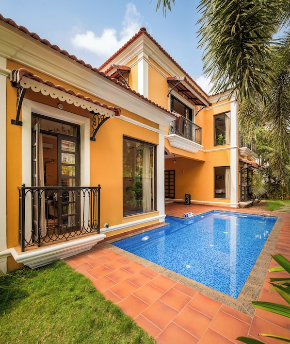 A two-story house with a swimming pool, a balcony, and a garden.