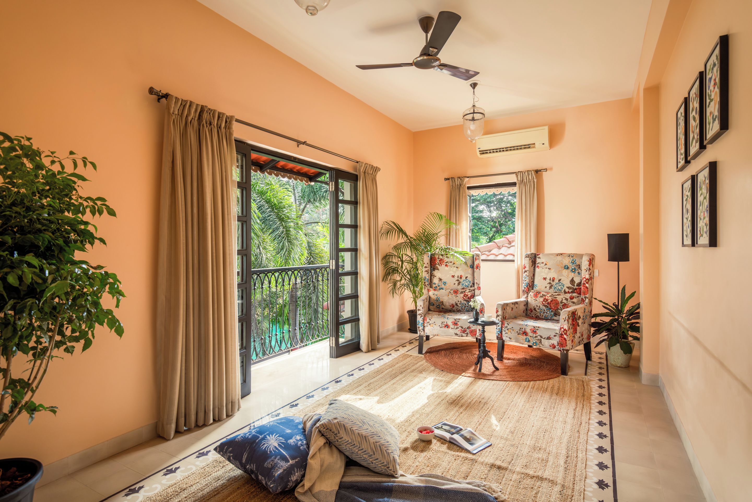 A room with a balcony, a ceiling fan, a potted plant, a chair, and a table with a book and a bowl.