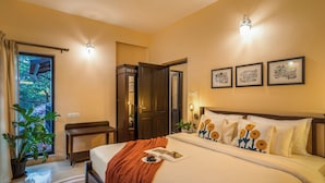 Habitación de hotel con cama, mesita de noche, silla, planta en maceta y puerta que da a un balcón.