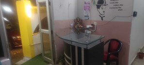 A room with a glass-top desk, a red chair, a small statue, and a wall with a poster. - Hotel Utsav & Resto Cafe (Dehradun)