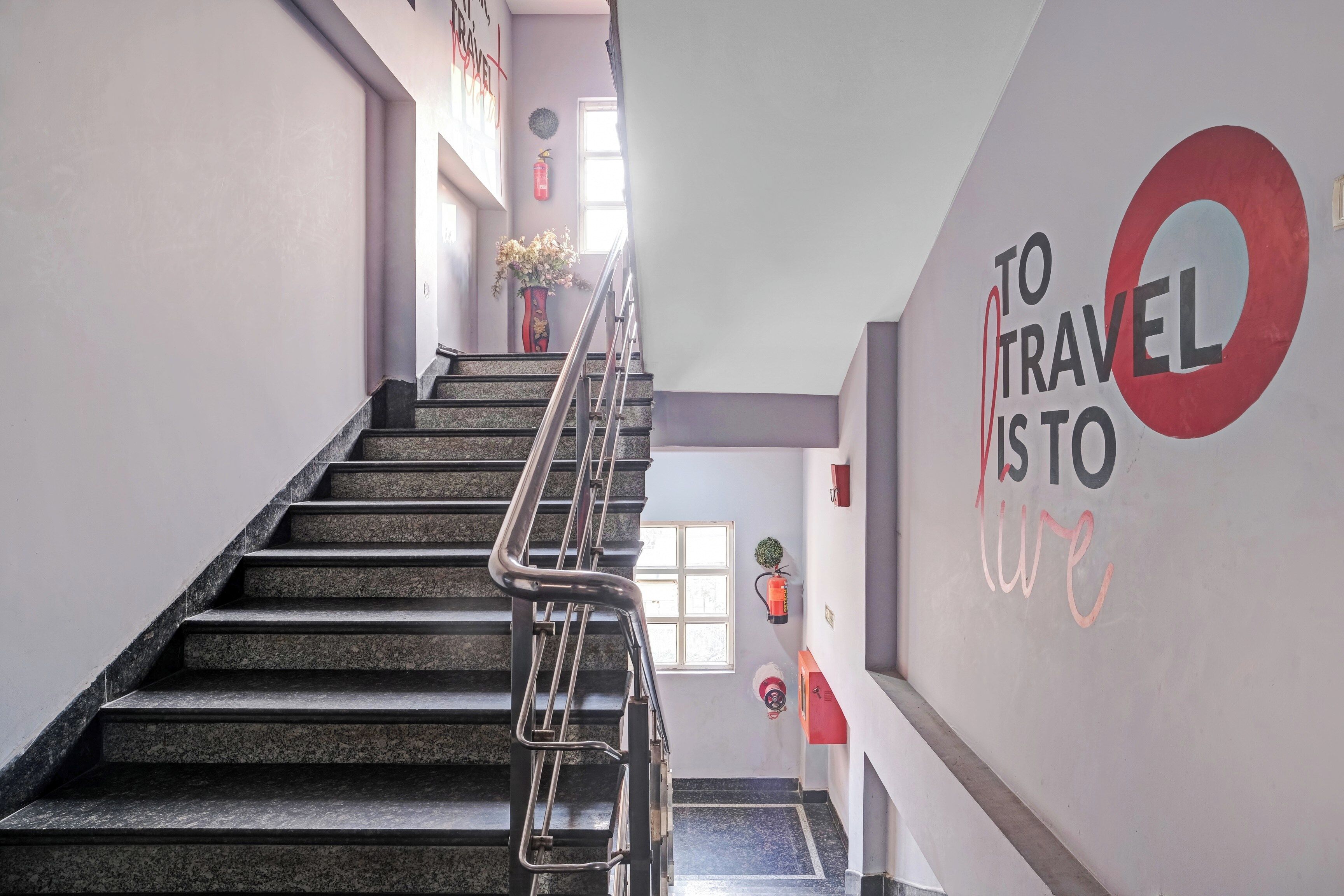 Uma escadaria com corrimãos de metal leva a um patamar com uma placa na parede que diz 'TO TRAVEL TO LIVE'.