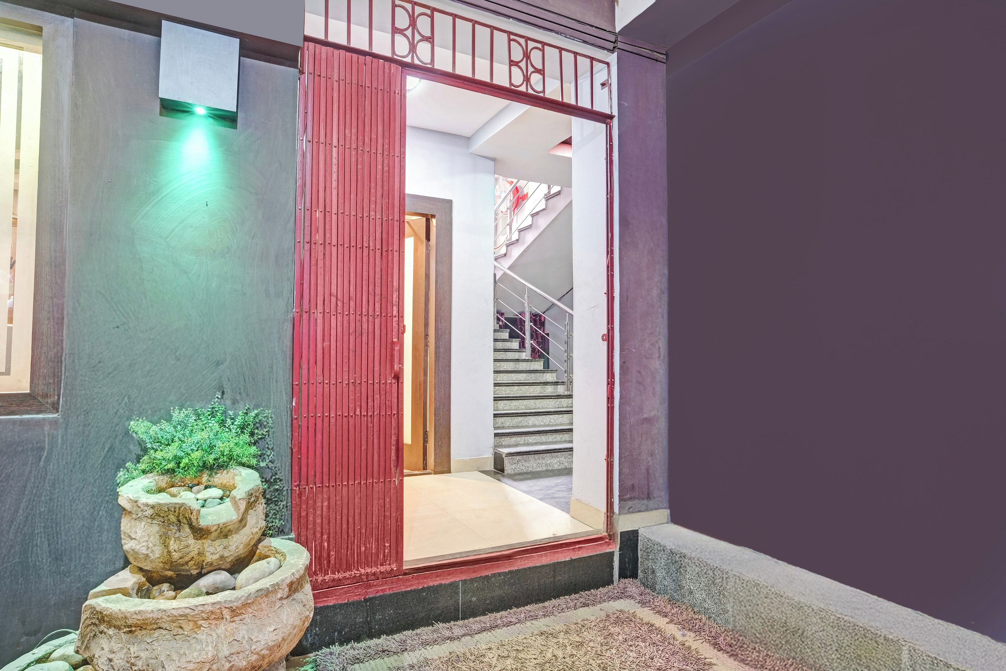 Entrada de hotel con una reja roja, una escalera y una jardinera de piedra con plantas verdes.