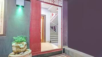Entrada de hotel con una reja roja, una escalera y una jardinera de piedra con plantas verdes.