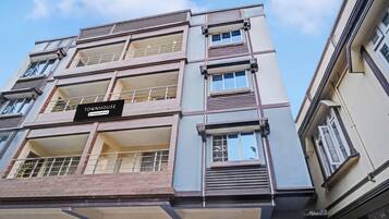 Un edificio de varios pisos con balcones, un cartel que indica que es propiedad de una empresa con servicios, y un cielo despejado al fondo.