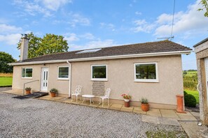 A single-story house with a tiled roof, a front door, and a small porch area with outdoor seating. - Willow Bank, Low Row, bungalow with stunning countryside views to Hadrian's Wall (Low Row)