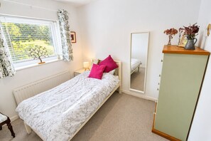 A bedroom with a single bed, a nightstand, a mirror, a radiator, a window with curtains, and a small table with a vase. - Willow Bank, Low Row, bungalow with stunning countryside views to Hadrian's Wall (Low Row)