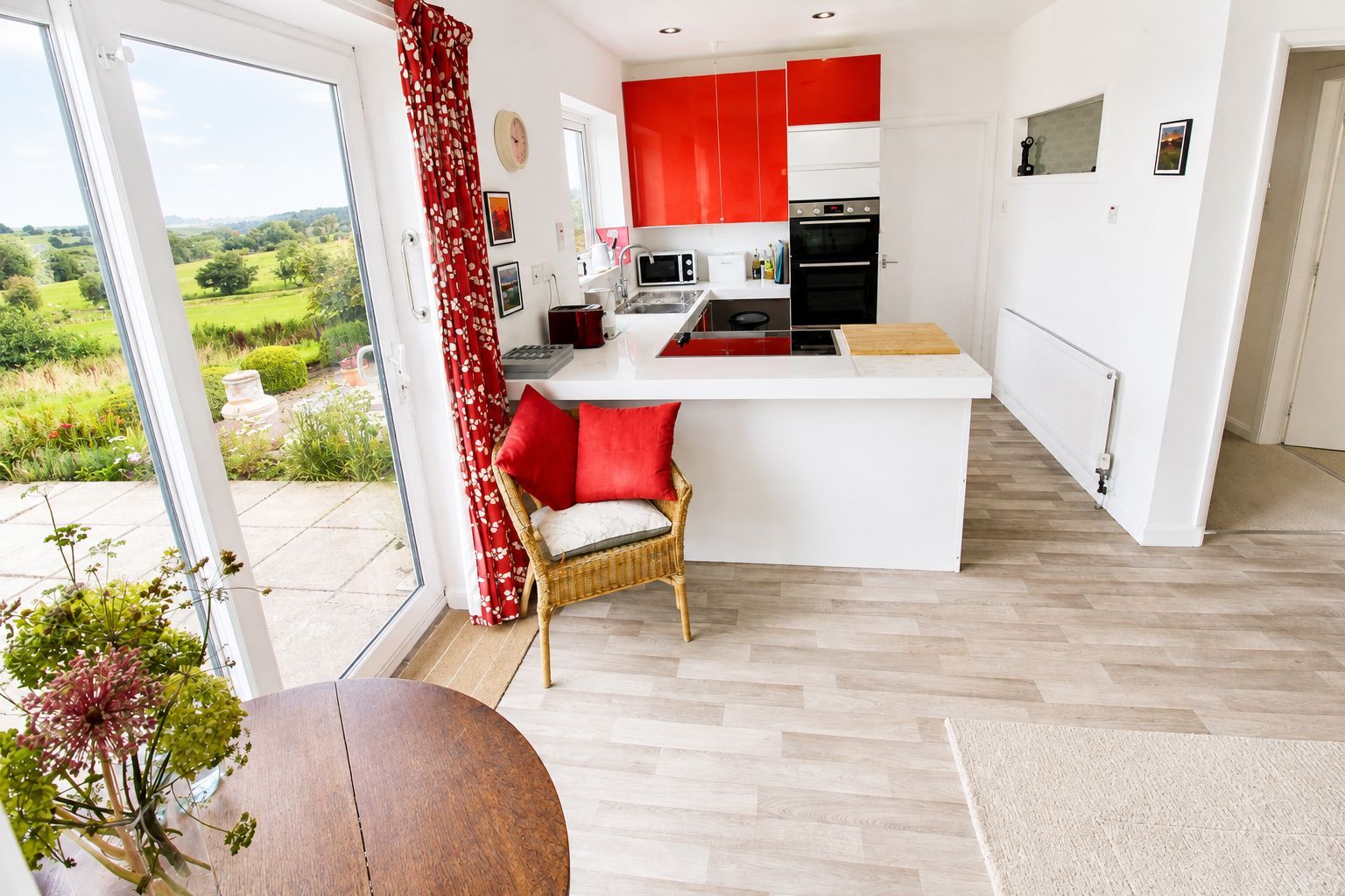 Een moderne keuken met rode kastjes, een wit aanrecht en uitzicht op een groen landschap.