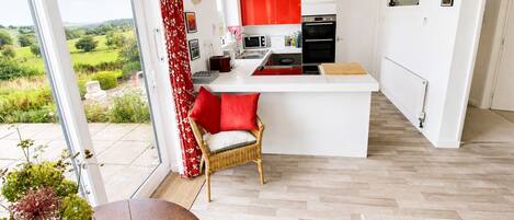 A modern kitchen with red cabinets, a white countertop, and a view of a green landscape.