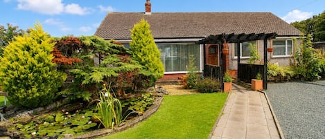 Una casa con un jardín bien cuidado, un estanque con nenúfares y un cielo azul despejado.