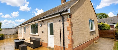 A two-story house with a tiled patio, a brick chimney, and a white door.