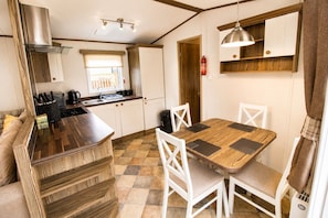 A compact kitchen with a central island, white cabinetry, and a dining area with a wooden table and chairs. - Calf Lonning Caravan, Plumbland, in a quiet Cumbrian village close to Keswick and Western Lakes (Plumbland)