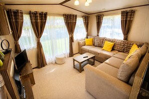 A cozy living room with a sofa, ottoman, and coffee table, featuring plaid curtains and a television. - Calf Lonning Caravan, Plumbland, in a quiet Cumbrian village close to Keswick and Western Lakes (Plumbland)
