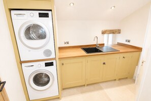 A compact kitchen with a washing machine, a sink, and wooden cabinets. - Stonethwaite, Dalston - a luxurious, dog friendly, romantic barn conversion (Dalston)