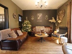 Una sala acogedora con un árbol de Navidad, sofás de cuero, una mesa de centro y un sillón.