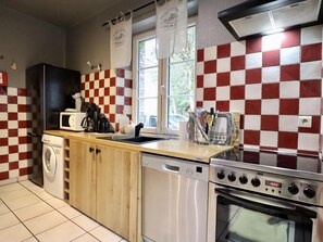 A kitchen with a red and white checkered backsplash, a washing machine, a dishwasher, a stove, and a window with curtains. - Pretty gite with terrace near the Semois river (Alle-sur-Semois)