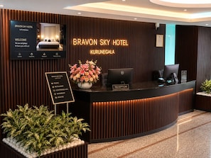A hotel reception desk with a digital display, a reception area, and a sign listing amenities. - Bravon Sky Hotel (Kurunegala)