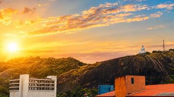 A cityscape with a large Buddha statue on a hill, buildings in the foreground, and a sunset.