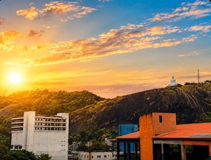 A cityscape with a large Buddha statue on a hill, buildings in the foreground, and a sunset.