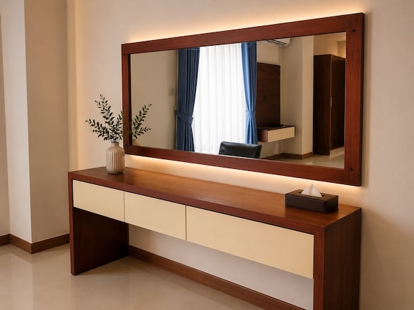 A modern vanity with a mirror, a vase with greenery, and a tissue box.