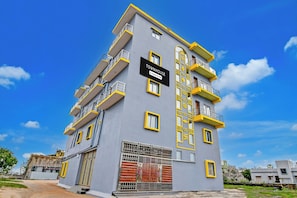 Un immeuble à plusieurs étages doté de balcons, une enseigne indiquant qu’il s’agit d’une maison de ville gérée par une entreprise, et une entrée sécurisée par un portail.