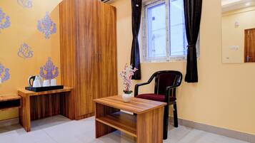 Una habitación con un armario de madera, una mesita con un jarrón de flores, una silla y una ventana con cortinas.