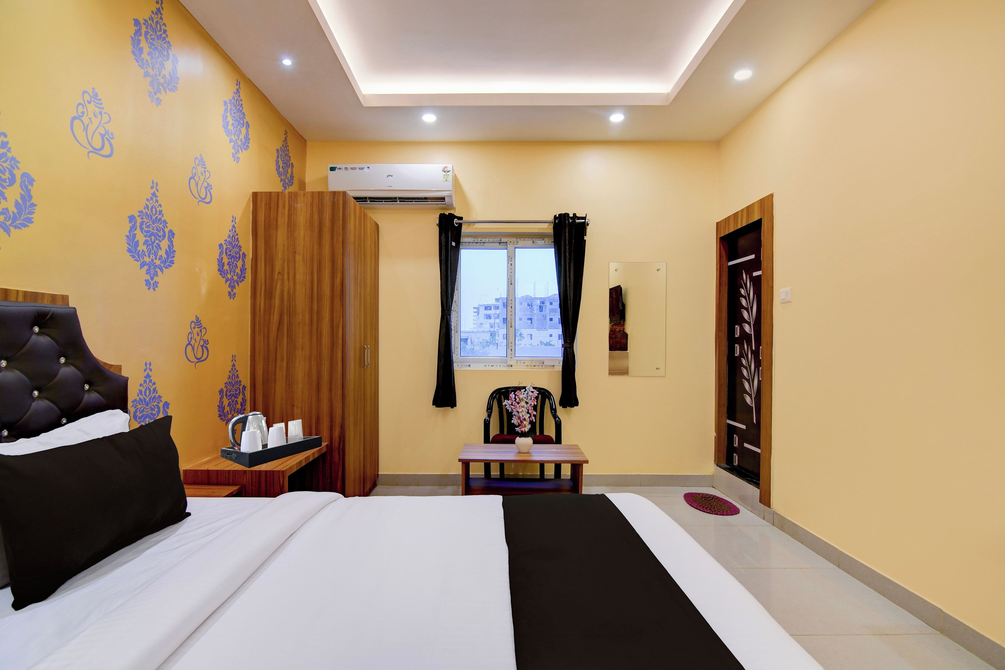 Habitación de hotel con cama, mesita de noche con tetera y tazas, una silla, ventana con cortinas y armario.
