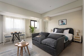 A modern bedroom with a grey sofa, a small dining table with chairs, a bedside lamp, and a framed picture on the wall. - Relax at bait assel by spacey #102 (cairo)