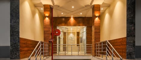 A hotel entrance with a modern design, featuring a central staircase with metal railings, a wooden wall, and a ceiling with recessed lighting.